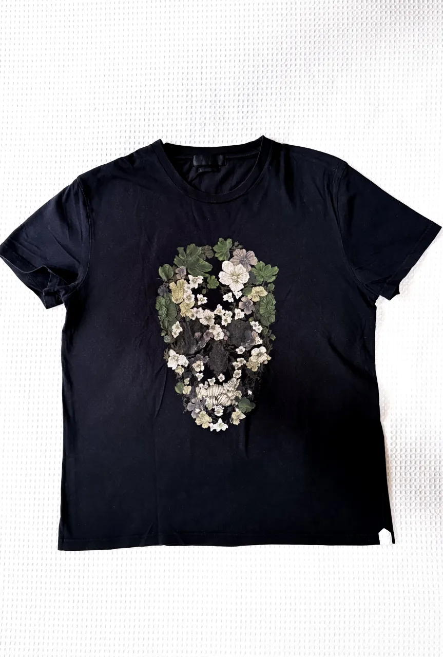 Remera Alexander McQueen color negra con estampa de calavera intervenida con flores y hojas en tonos verdes y blancos. La estampa se ubica en el frente de la prenda, y a un margen la leyenda “Alexander McQueen”  estampado.
Talle L.
medida de sisa: 54cm. 
Estado de la prenda: usado.