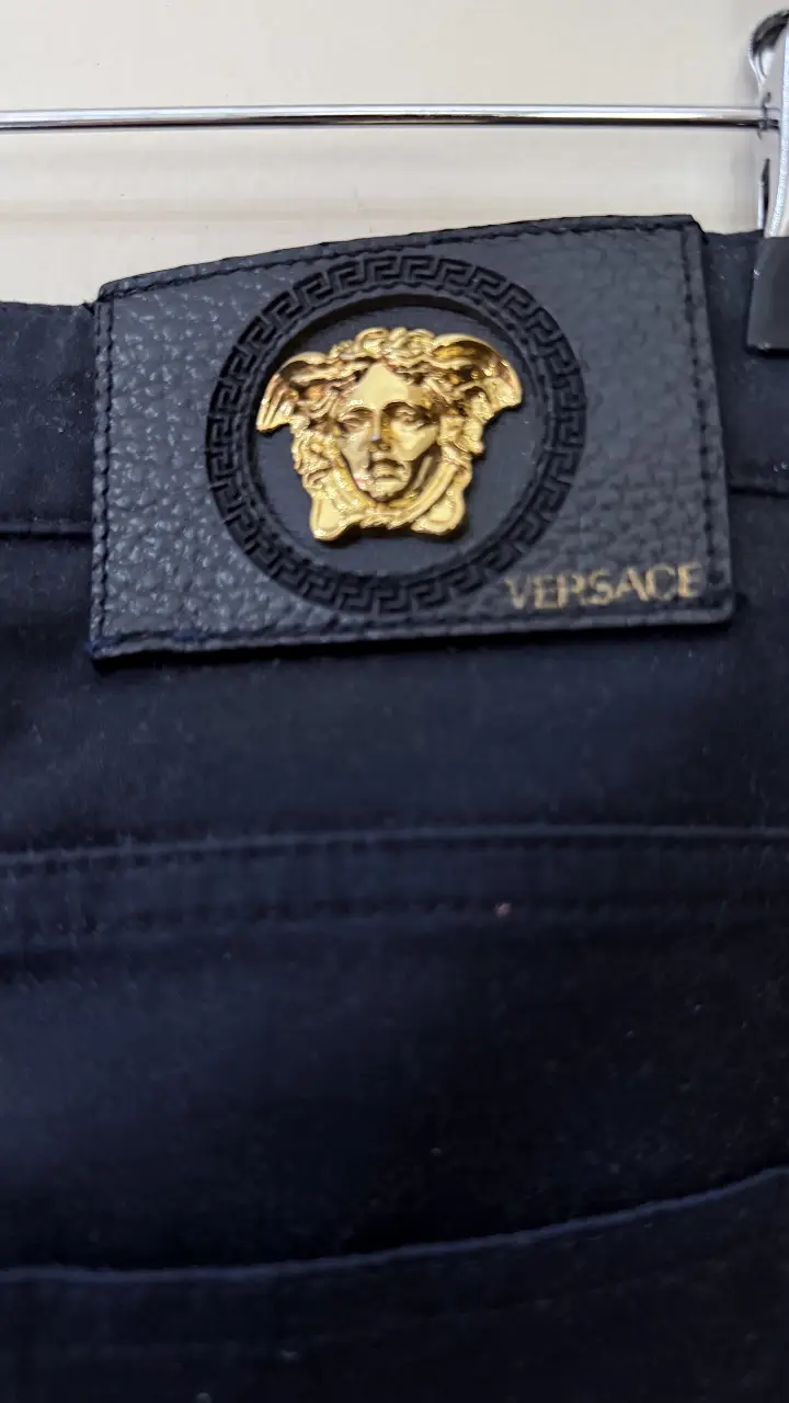 Jeans rectos de hombre, color azul oscuro, con detalle de etiqueta de cuero con logo de la marca Versace. Un clásico atemporal para cualquier guardarropa. 