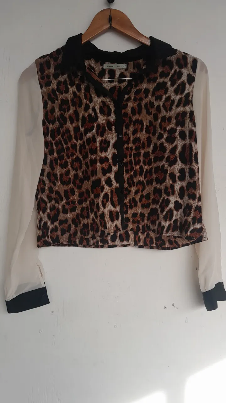 Blusa de mujer con estampado de leopardo y mangas transparentes. Cuello y puños negros. Ideal para un look moderno y sofisticado.