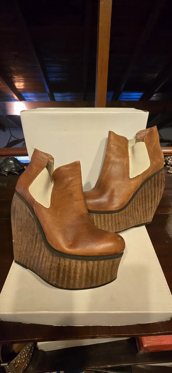 Botitas Satori de cuero color suela, con plataforma y taco cuña de madera trabajada. Tienen elástico a los costados crudos 