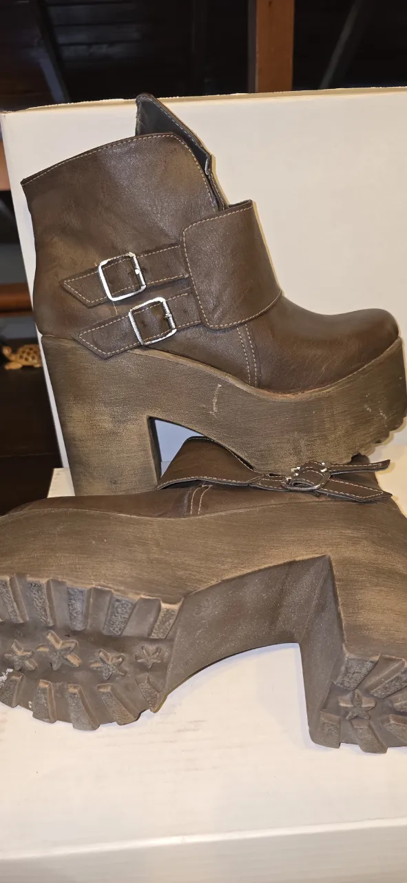Botas tipo borcegos, marrones con plataforma alta y taco de madera. Tienen dos hebillas metálicas en la parte superior.
