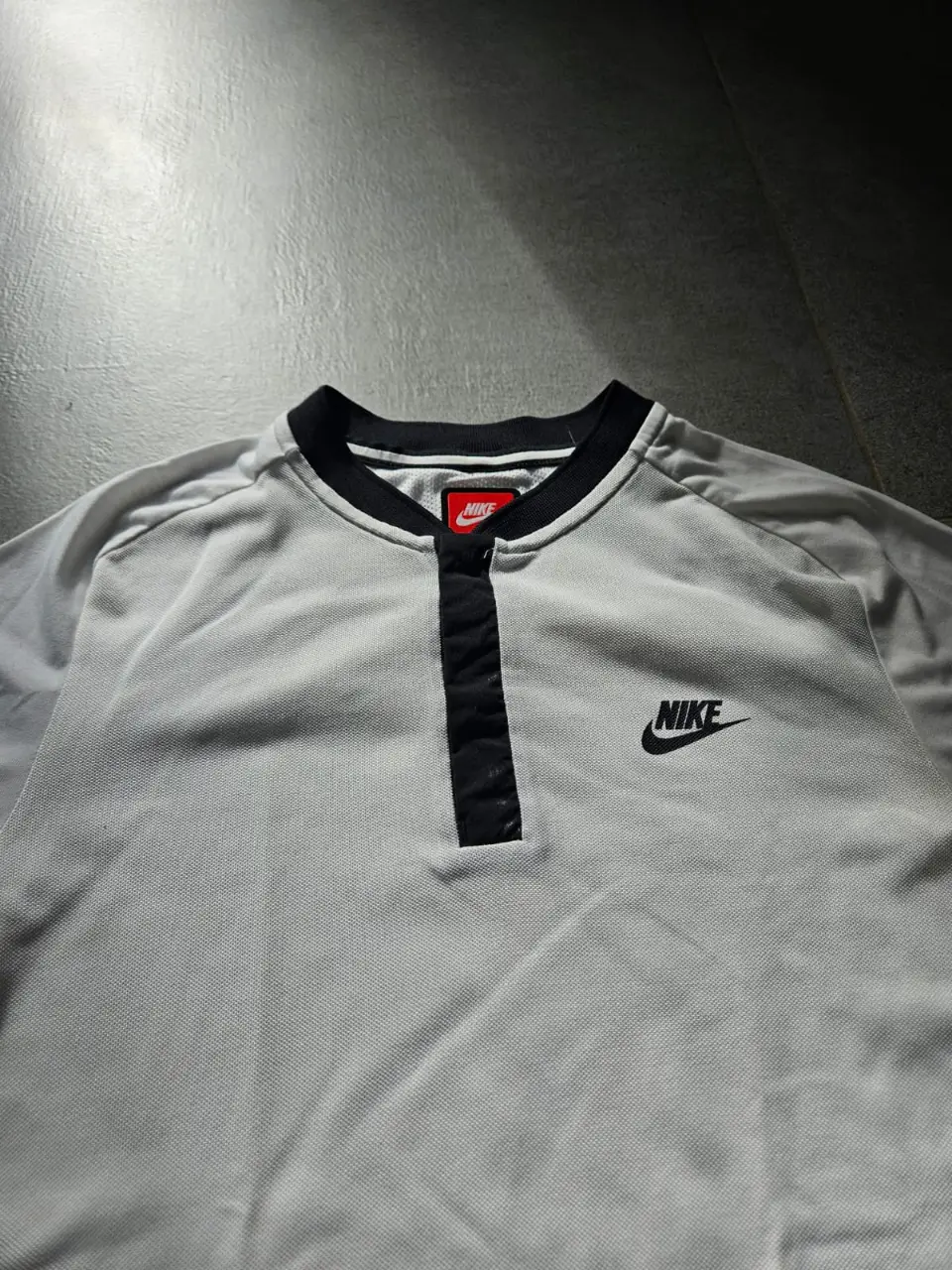 Remera deportiva Nike blanca con detalles en negro. Cuello redondo con solapa y botones. Logo Nike bordado.