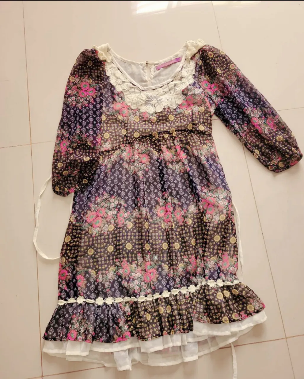 Vestido forrado estampado floral con cuello de encaje blanco y volado en la falda. Mangas al codo con puños fruncidos. Posee cintas para atar en la cintura.