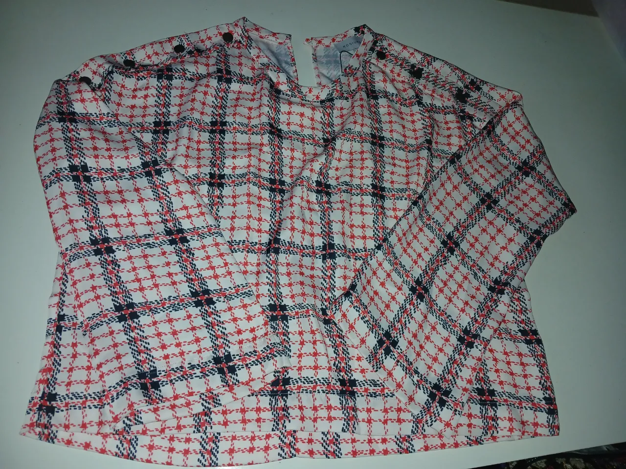 Blusa blanca con estampa escocesa en rojo, azul y negro. Tiene botones en los hombros. Figura talle S pero puse único porque va hasta un L. El modelo es overzice. La tela tiene mucha caída y no cede, es una blusa. 