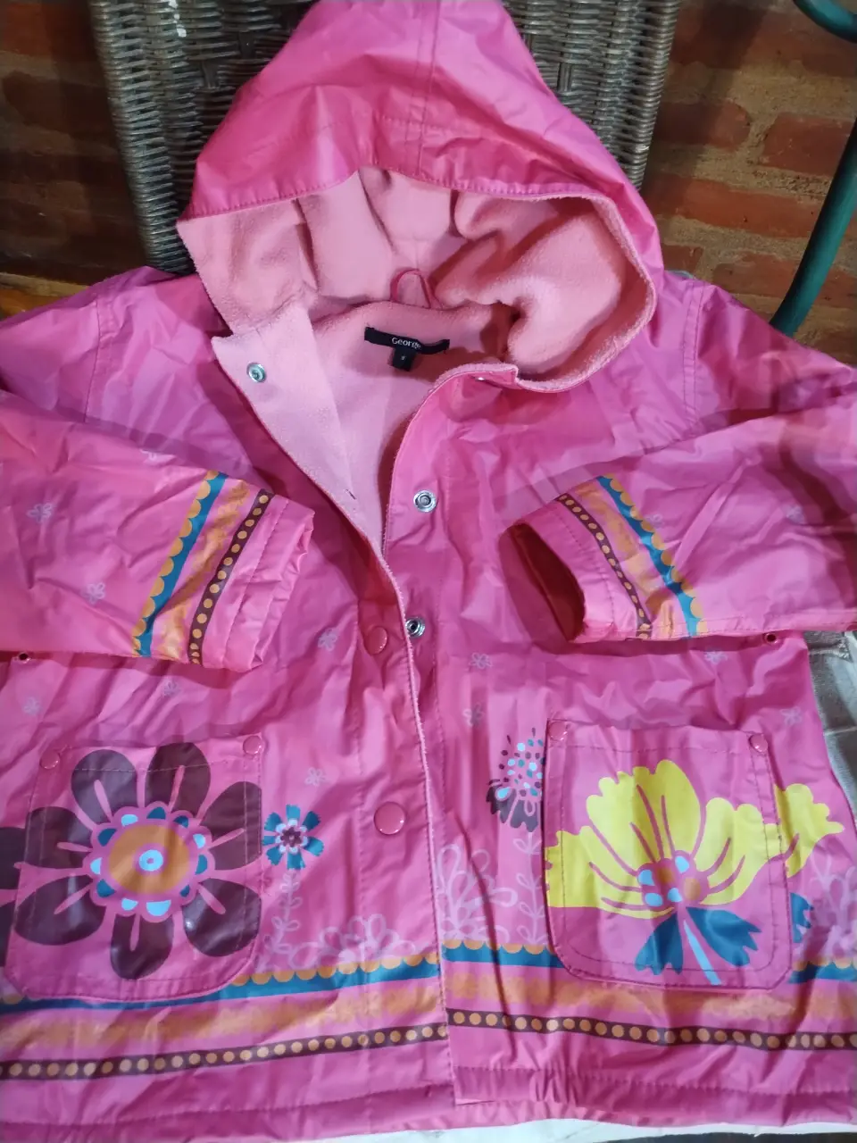 Chaqueta impermeable rosa para niña, con capucha y detalles florales. Ideal para días de lluvia.