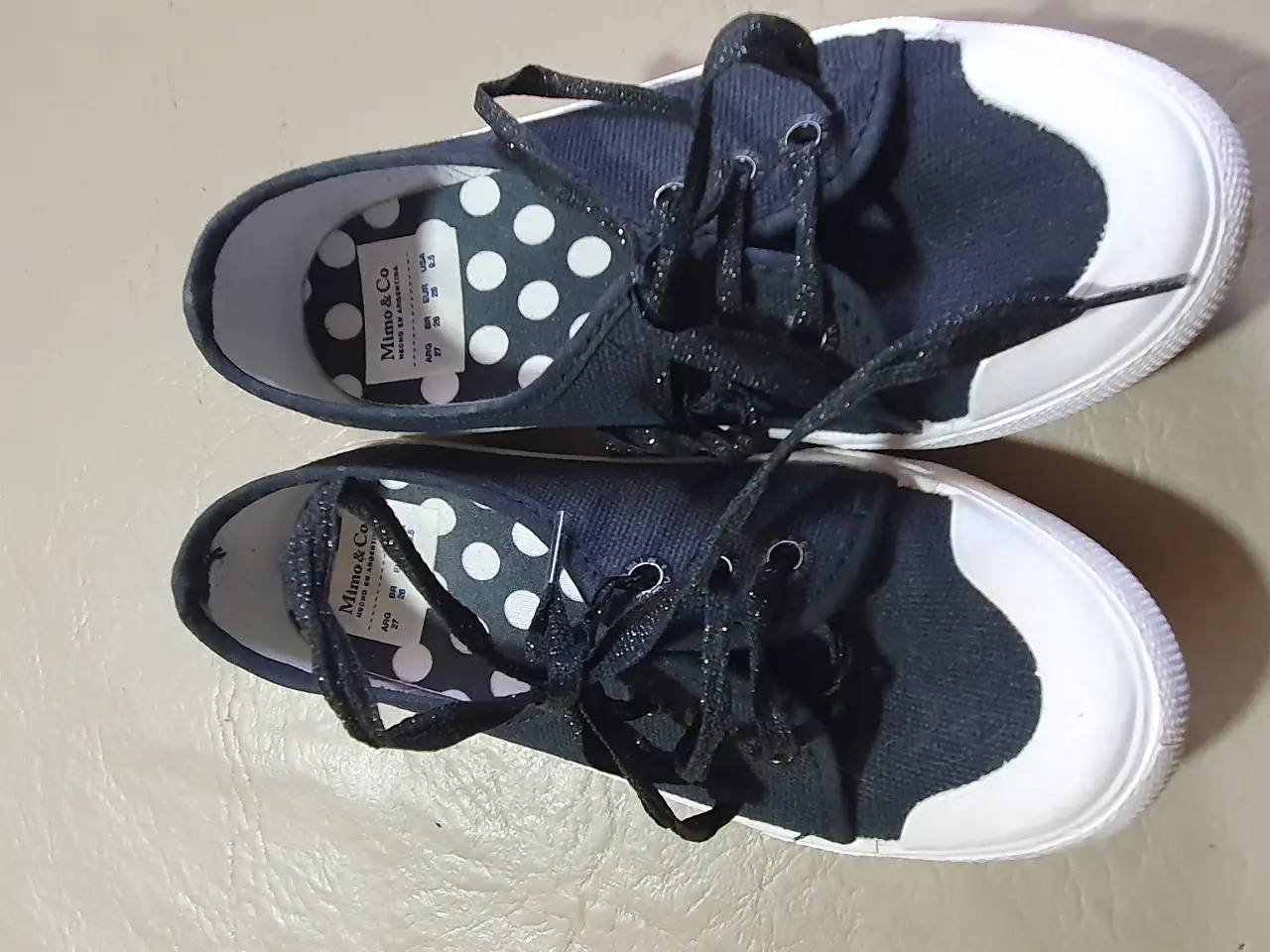 Zapatillas de lona negras con puntera blanca y detalles brillantes en los cordones. Diseño clásico y cómodo, ideales para un look casual y versátil.