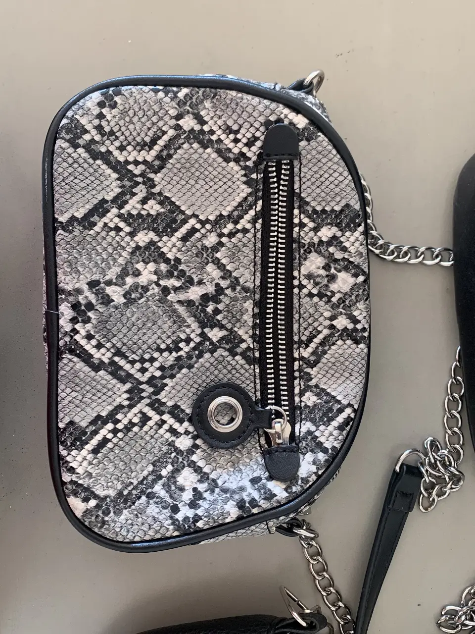 Cartera bandolera con estampado de serpiente, cierre y cadena plateada.