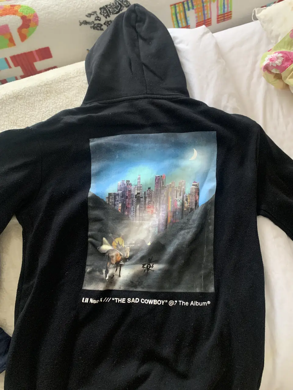 Buzo canguro negro con capucha, estampado en la espalda con diseño de Lil Nas X y su álbum "The Sad Cowboy". Estilo streetwear y cómodo para uso diario.