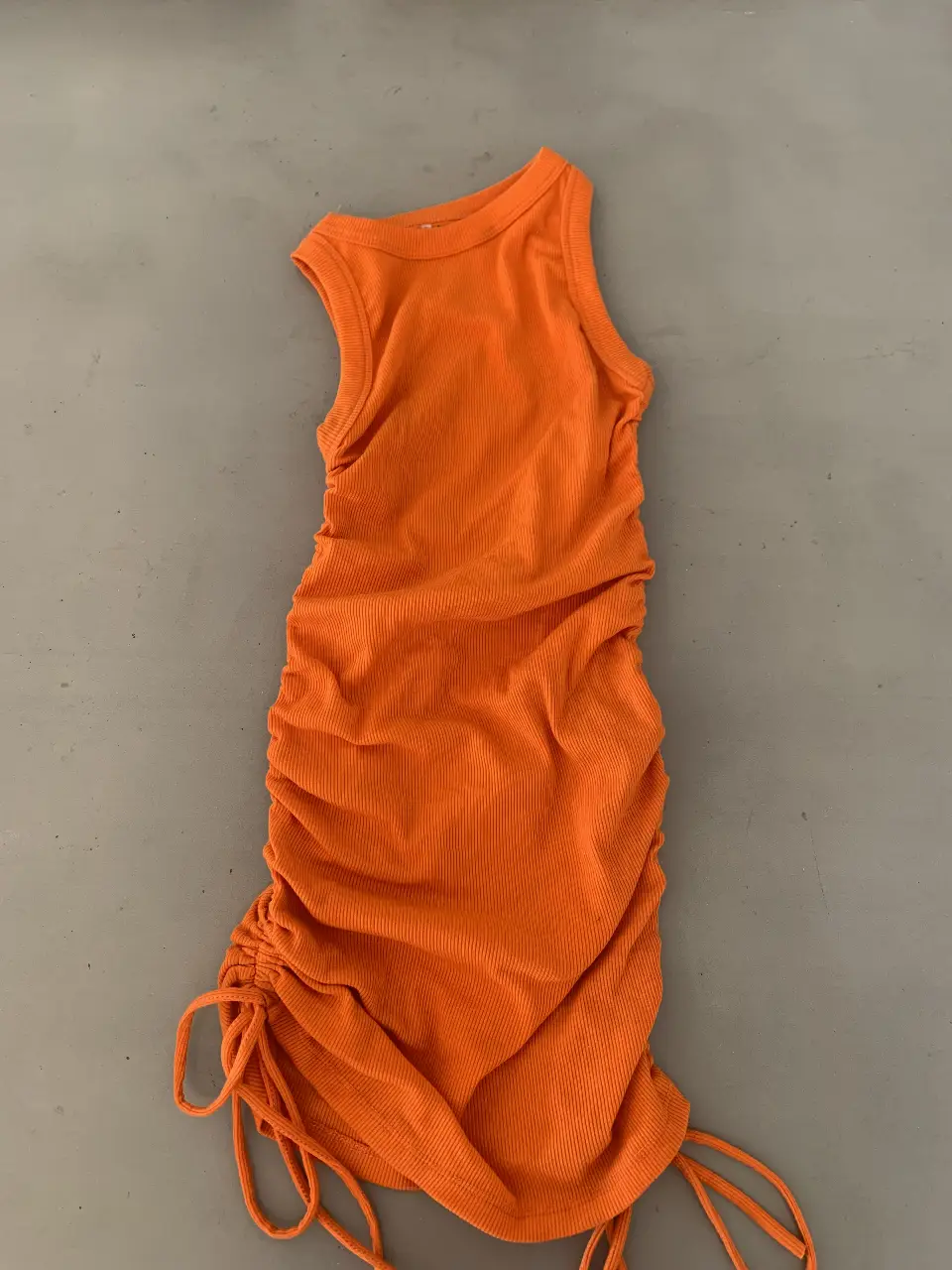 Vestido mini naranja con frunces laterales y tiras ajustables. Ideal para un look moderno y audaz.
