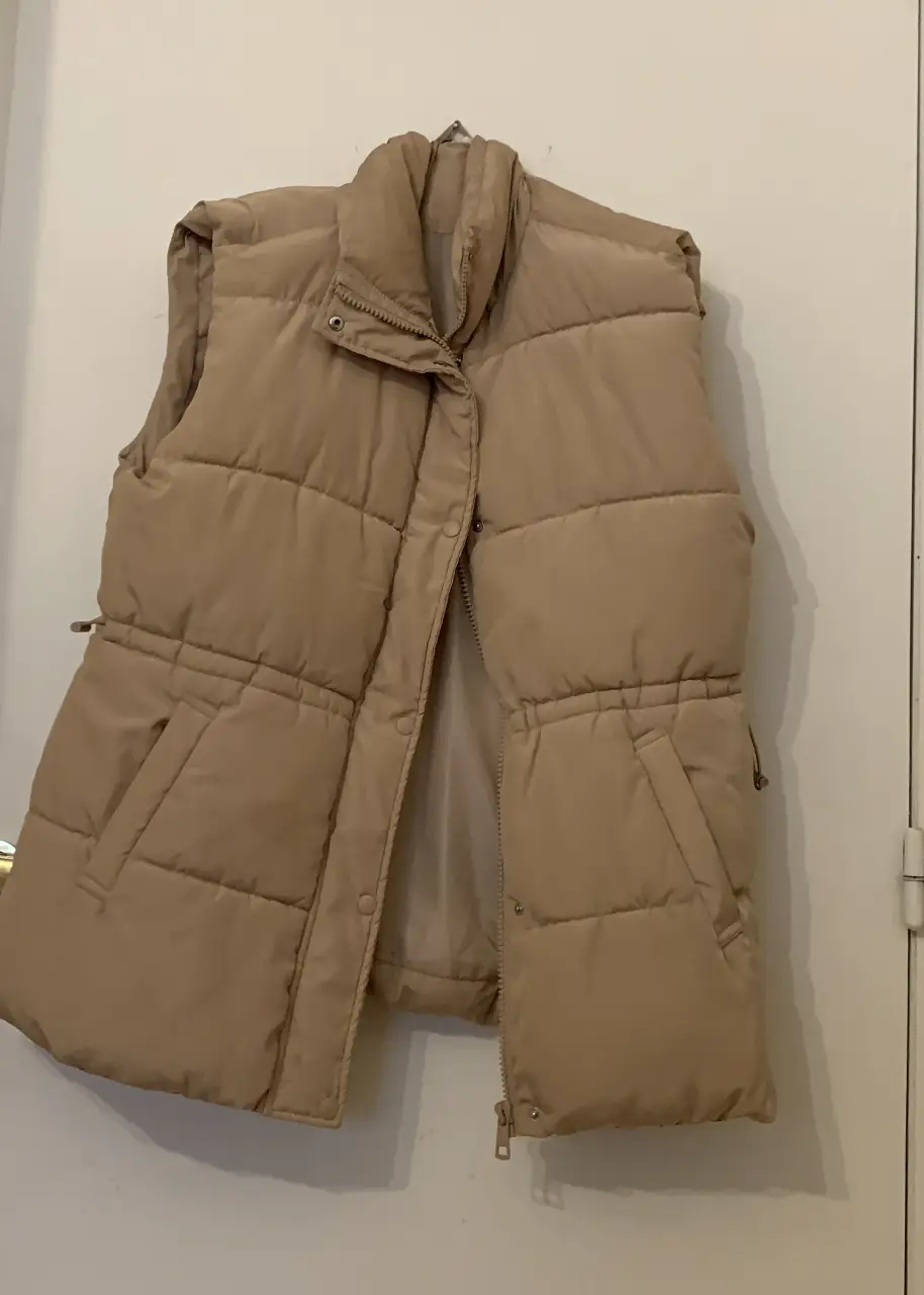 Chaleco puffer beige, ideal para el invierno. Confeccionado con materiales acolchados, cierre y bolsillos. Ajustable en la parte de la cintura.
