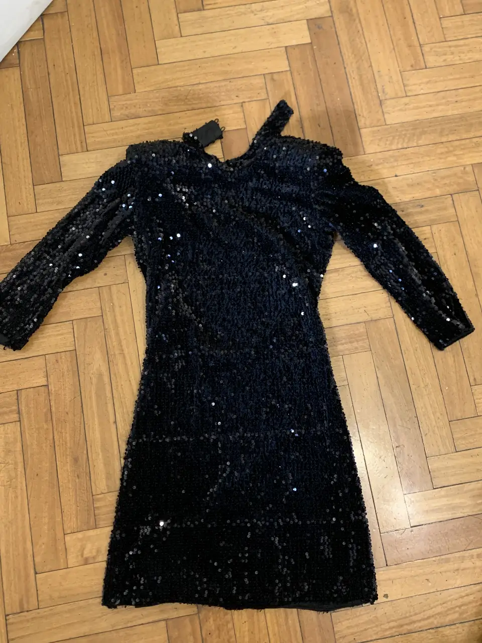 Vestido mini negro con lentejuelas, ideal para fiestas y eventos especiales. Diseño con un solo hombro y manga larga, perfecto para un look elegante y llamativo.