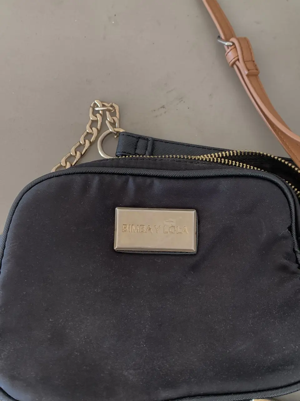 Cartera negra de la marca Bimba y Lola, con detalles dorados y cadena. Ideal para llevar lo esencial con estilo.