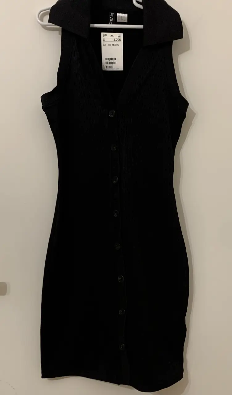 Vestido negro corto con cuello solapa y botones delanteros del principio al final. Ideal para un look elegante y versátil.