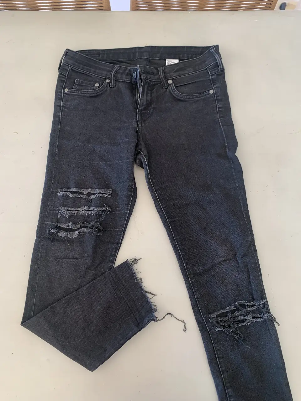 Jeans recto apretado negro de mujer/hombre con roturas en las rodillas y en el borde inferior. Tiro medio. Ideal para un look casual y moderno.