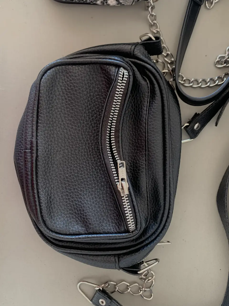 cartera negra con cierre y detalles de cadena. Ideal para llevar lo esencial con estilo.