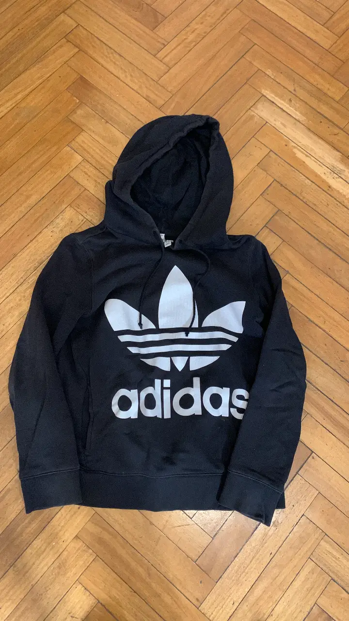 Buzo canguro Adidas negro con el logo icónico en blanco. Ideal para un look deportivo y casual. Perfecto para el día a día.