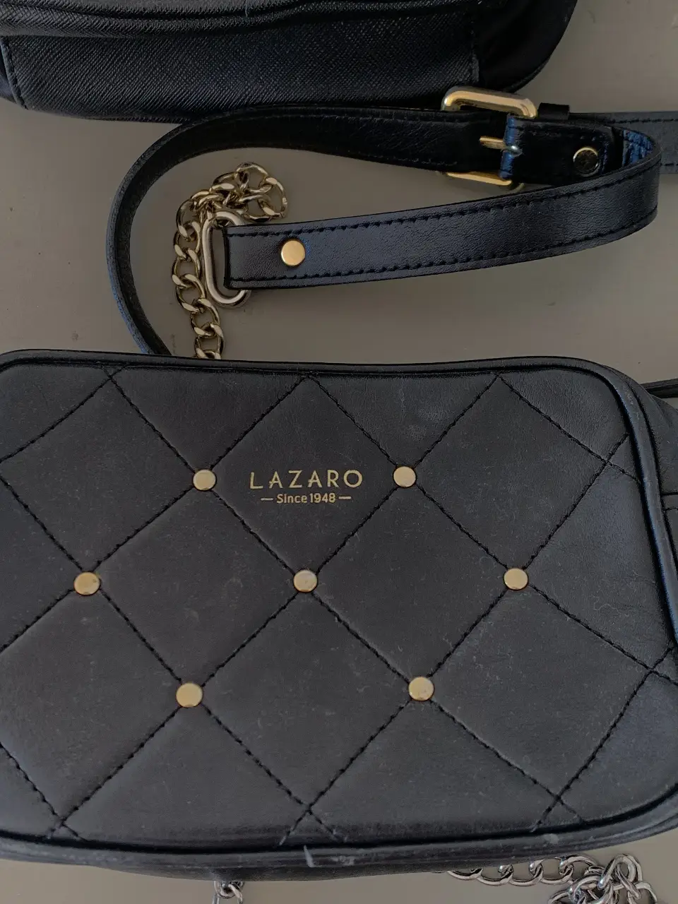 Cartera bandolera negra de cuero con diseño acolchado y detalles dorados. Ideal para un look elegante y moderno.