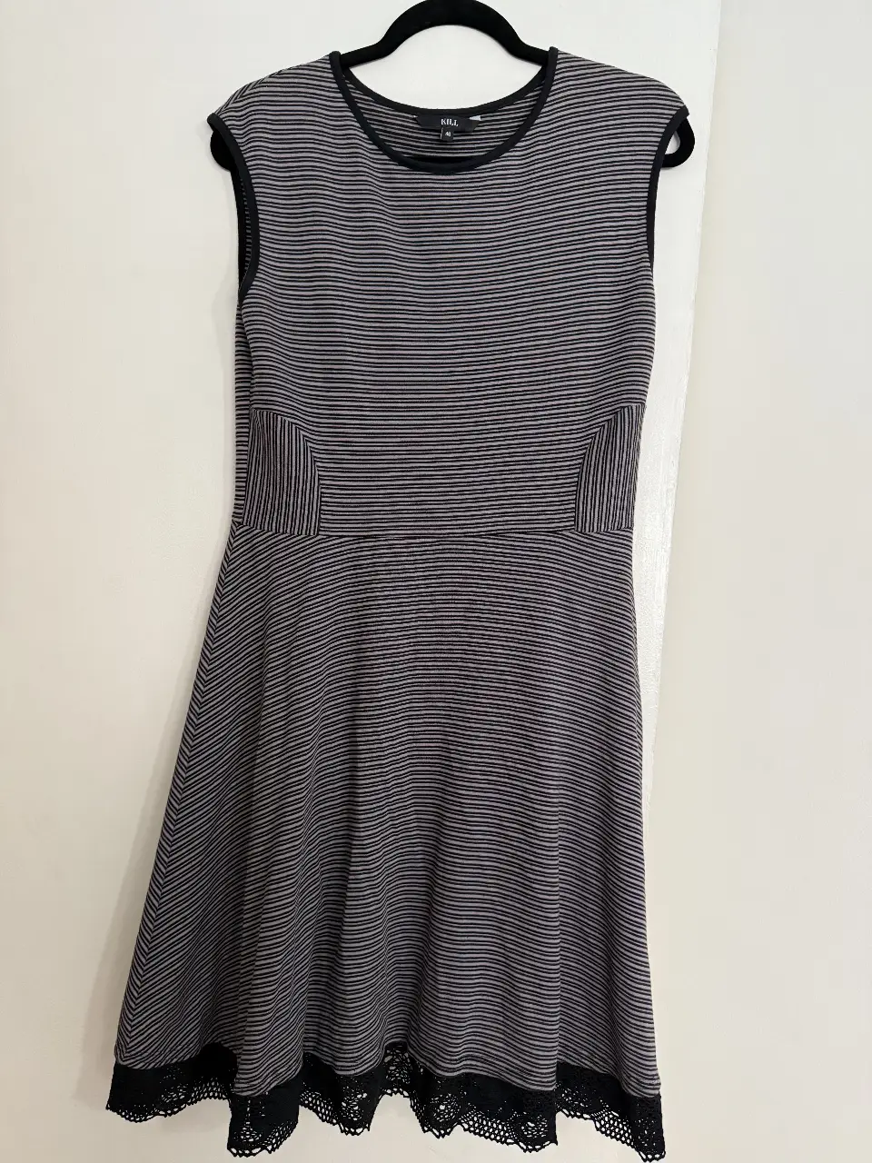 Vestido midi a rayas horizontales en tonos grises y negros. Diseño sin mangas con detalles en negro en cuello y sisas. Incluye detalles en los laterales y en el bajo con encaje negro. Ideal para un look casual y elegante.