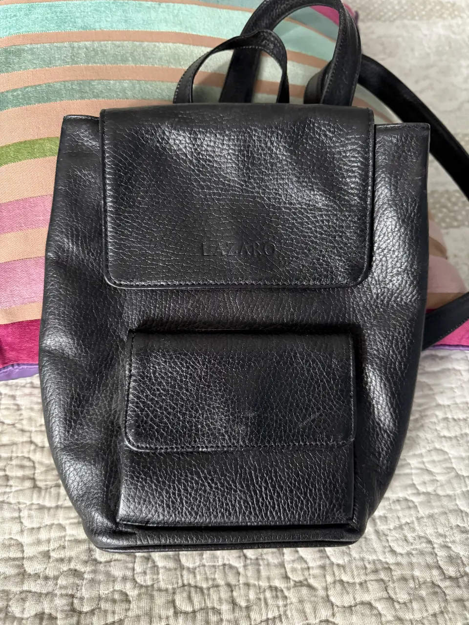Mochila negra de cuero, con solapa y bolsillo frontal. Ideal para uso diario.