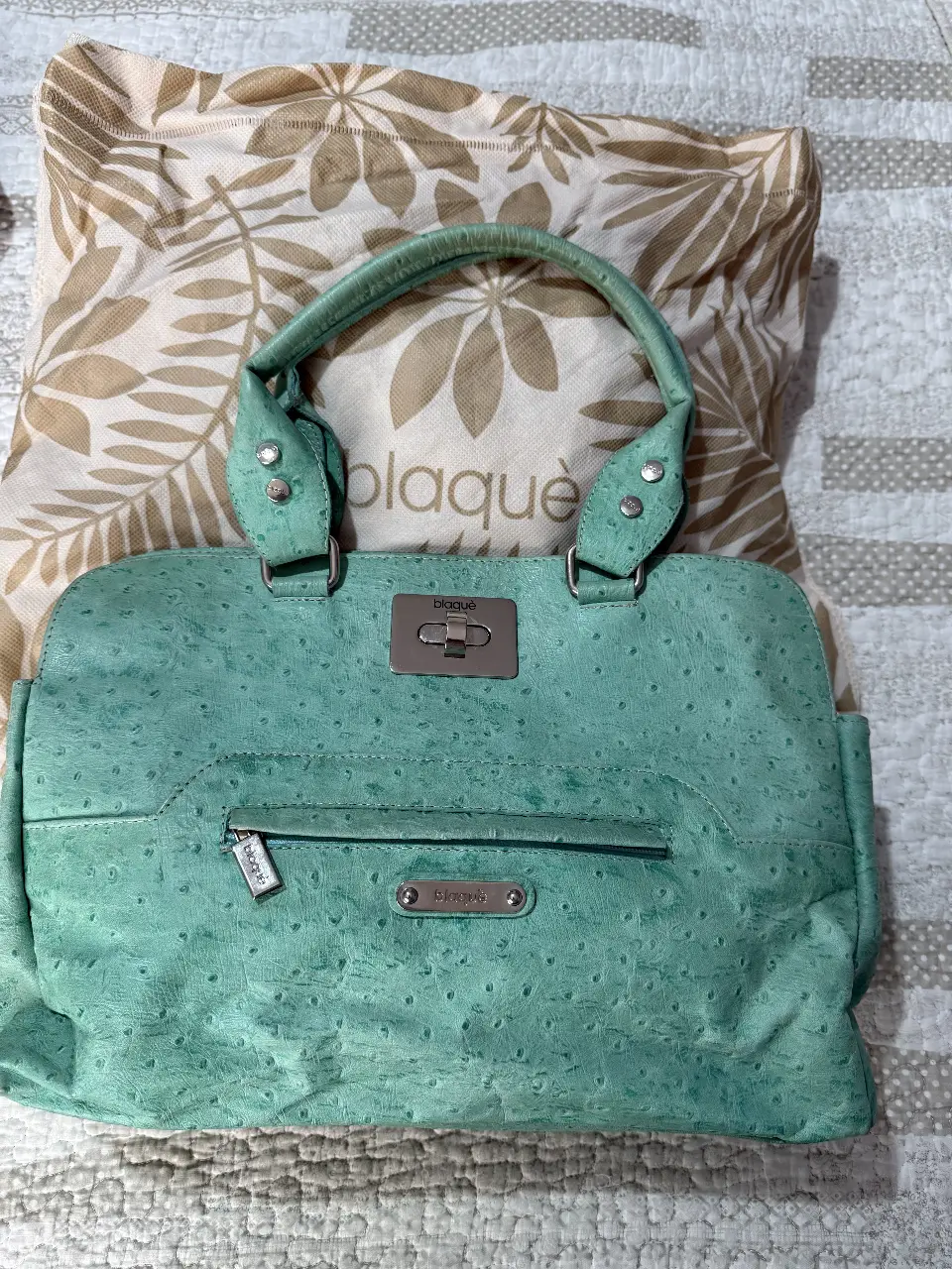 Cartera de mano de cuero verde agua con detalles plateados. Ideal para llevar tus esenciales con estilo. Tiene un bolsillo exterior con cierre y varios en el interior