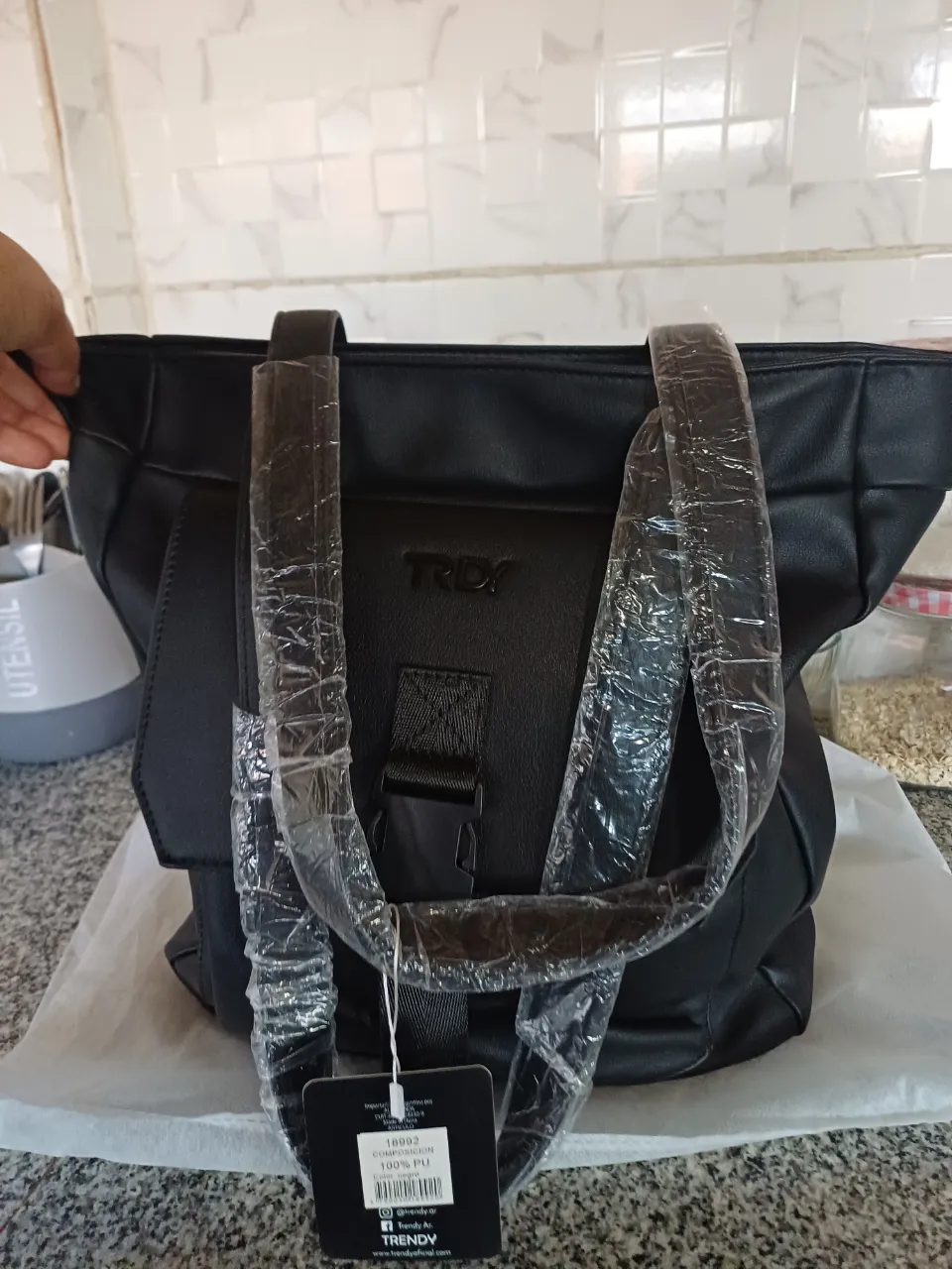 Bolso negro de cuero sintético con bolsillo frontal y hebilla. Interior forrado con estampado de corazones y logo.