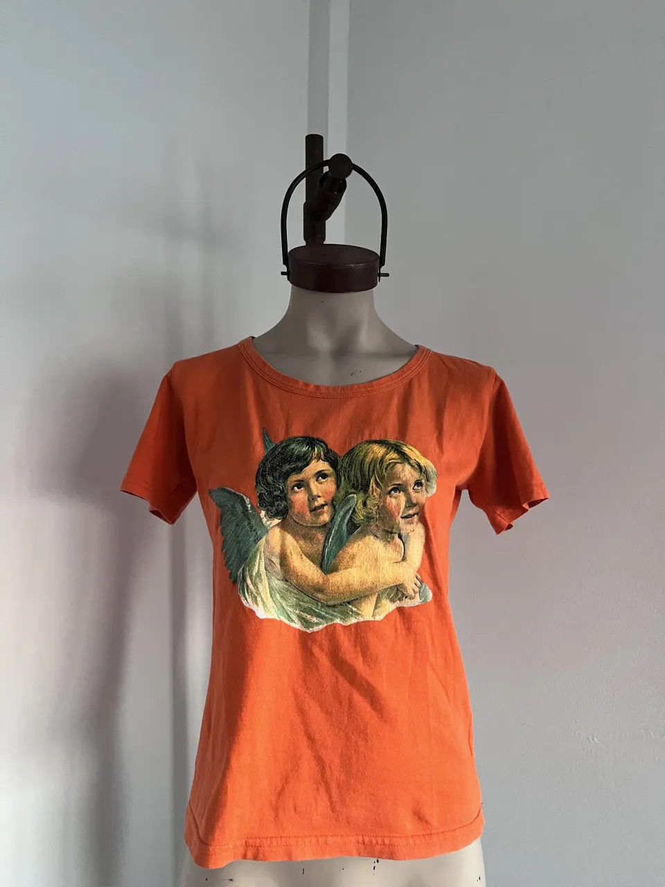 Remera naranja con estampa de dos angelitos abrazados en el frente. usada en excelente estado. medidas sisa 46 cm. largo 58 cm.