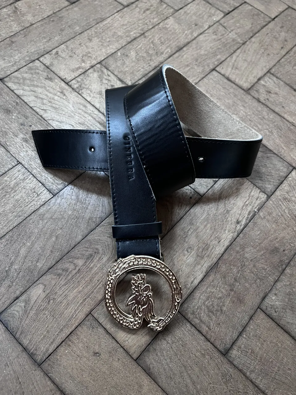 Cinturón negro de cuero con hebilla dorada con diseño de dragón.