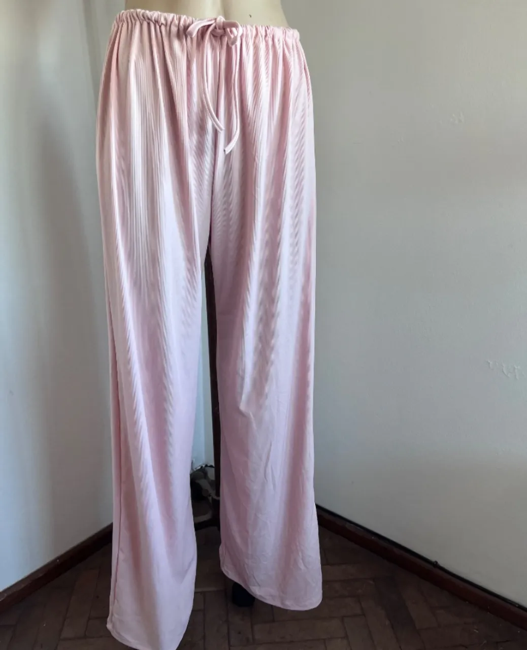 Pantalón de pijama rosa pastel, tiro alto, con cordón ajustable en la cintura. Diseño liso con finas rayas verticales sutiles. Piernas anchas y sueltas, ideal para estar cómoda en casa. nuevo. medidas cintura 32 a 46. cadera 65. largo 106.