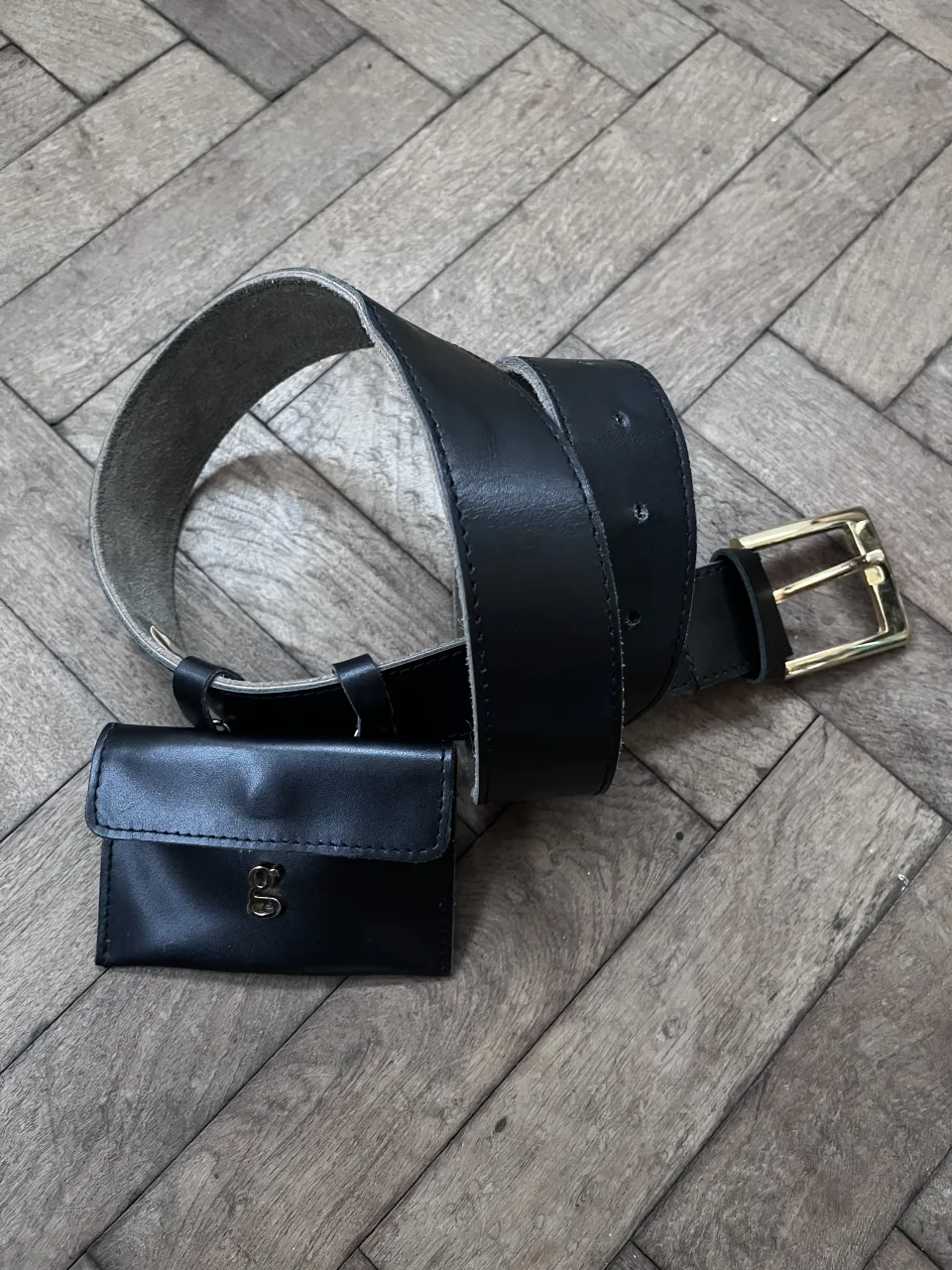 Cinturón negro de cuero con hebilla dorada y un pequeño monedero negro desmontable. El monedero tiene un logo dorado. usado, en buen estado, con mínimos detalles que se ven en la foto. largo 96 cm ancho 4 cm.