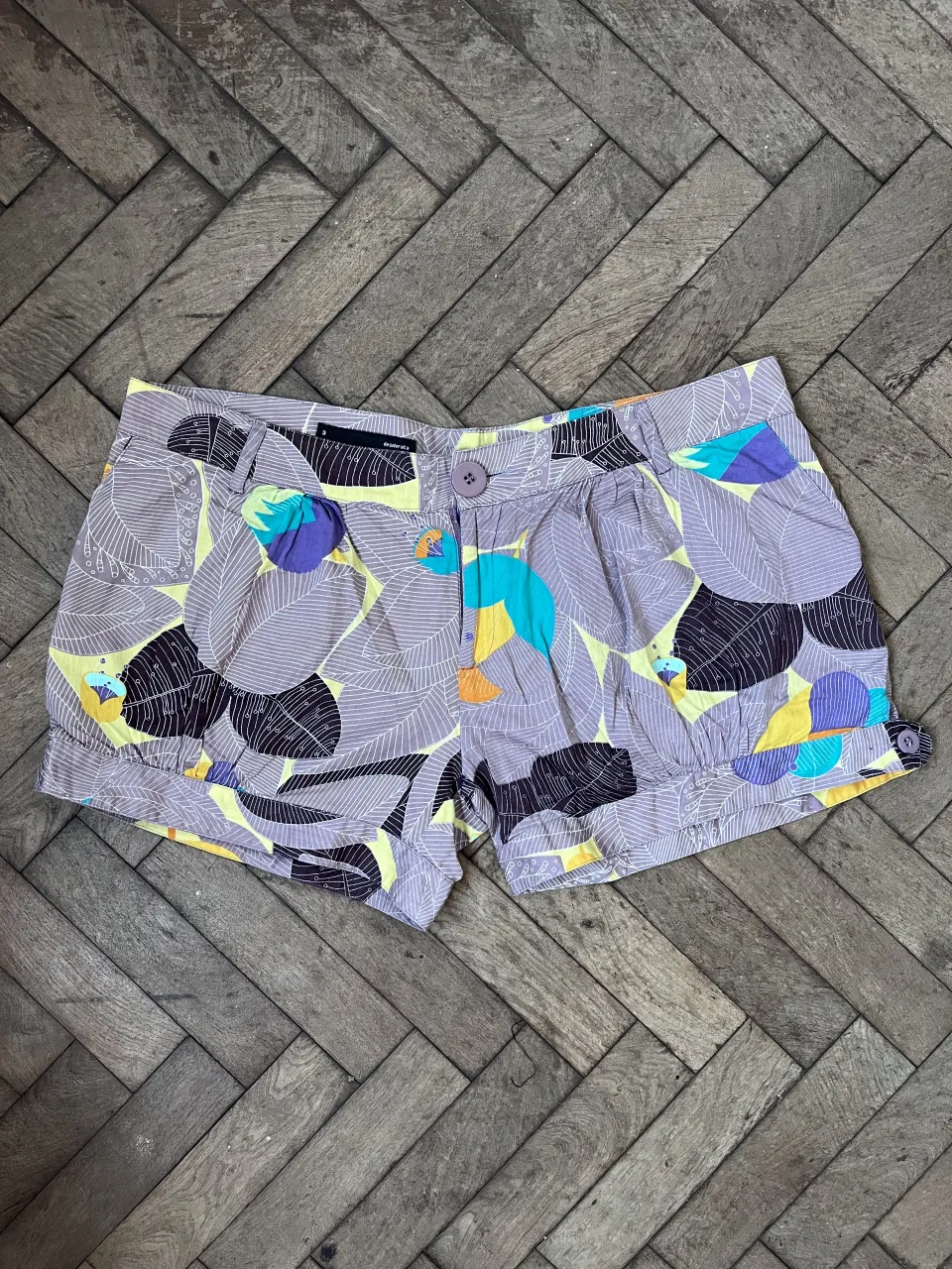Shorts de mujer con estampado floral y hojas en tonos lilas, amarillos, azules y naranjas. Tienen un corte clásico con bolsillos y detalles de botones. excelente estado. 100% algodón. medidas 45 cintura 60 cadera 28 largo.