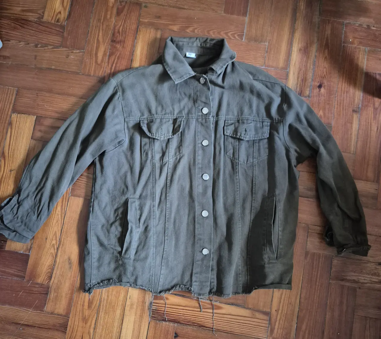 Campera de jean verde militar con detalles deshilachados en el borde inferior. Posee dos bolsillos delanteros con solapa y dos bolsillos laterales. Cierre con botones.