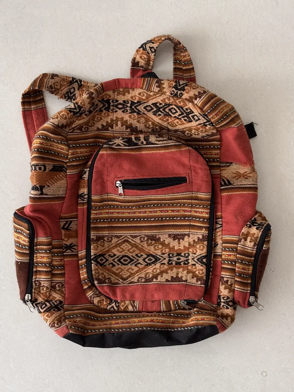 Mochila artesanal con diseño étnico en tonos rojos y marrones. Ideal para llevar tus cosas con estilo y un toque bohemio.
