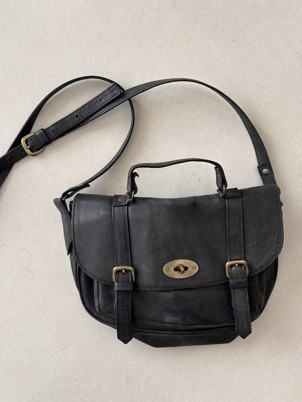 Cartera bandolera de cuero negro, con solapa y cierre de hebilla. Ideal para un look casual y versátil.
