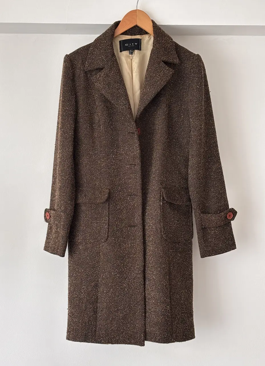 Elegante tapado largo de mujer, color marrón con textura tweed. Posee dos bolsillos frontales, botones en el frente y en los puños. Ideal para un look formal o de trabajo. Medida: contorno 100cm