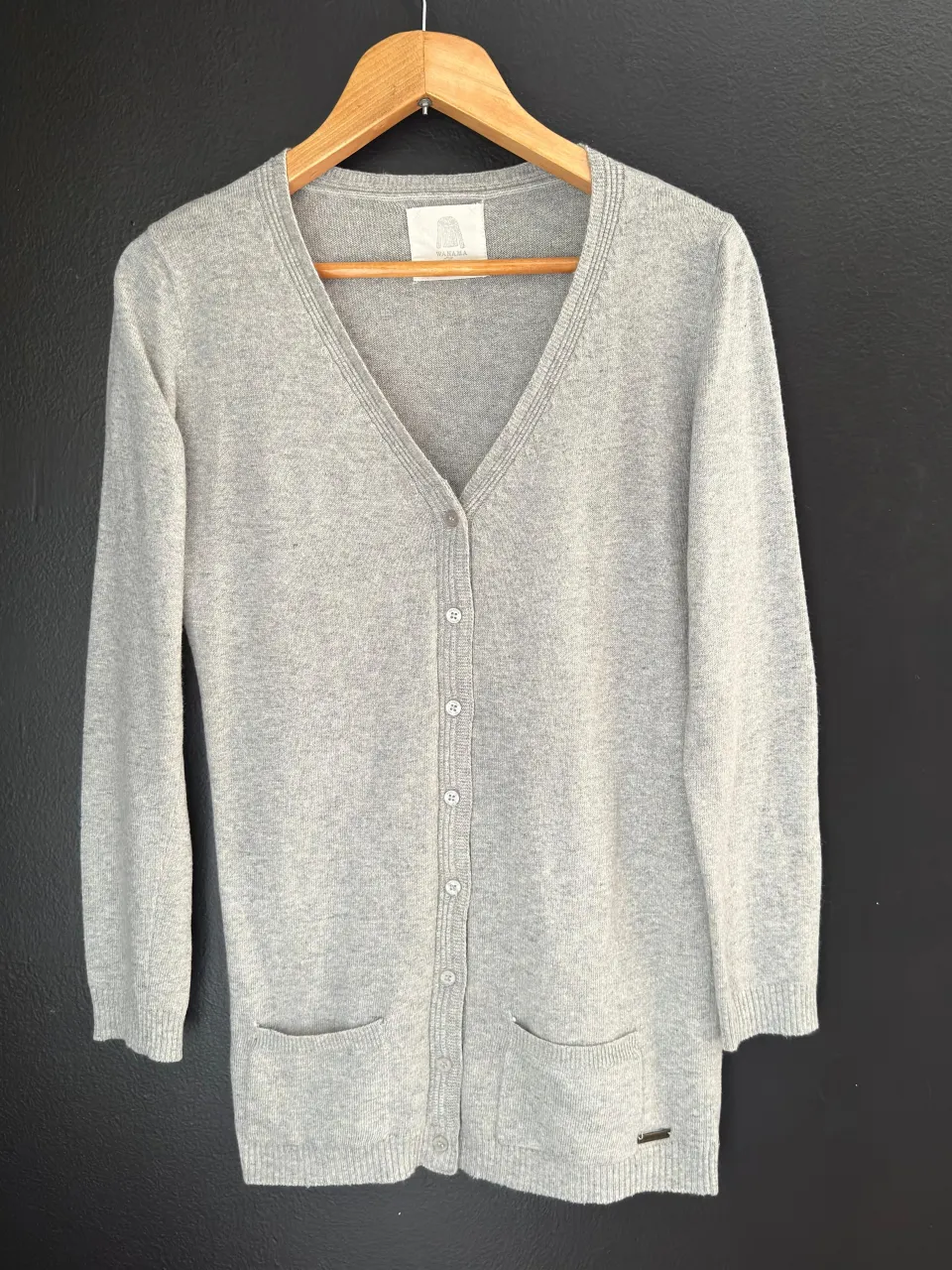 Cardigan gris con botones al frente y dos bolsillos inferiores. Cuello en V.