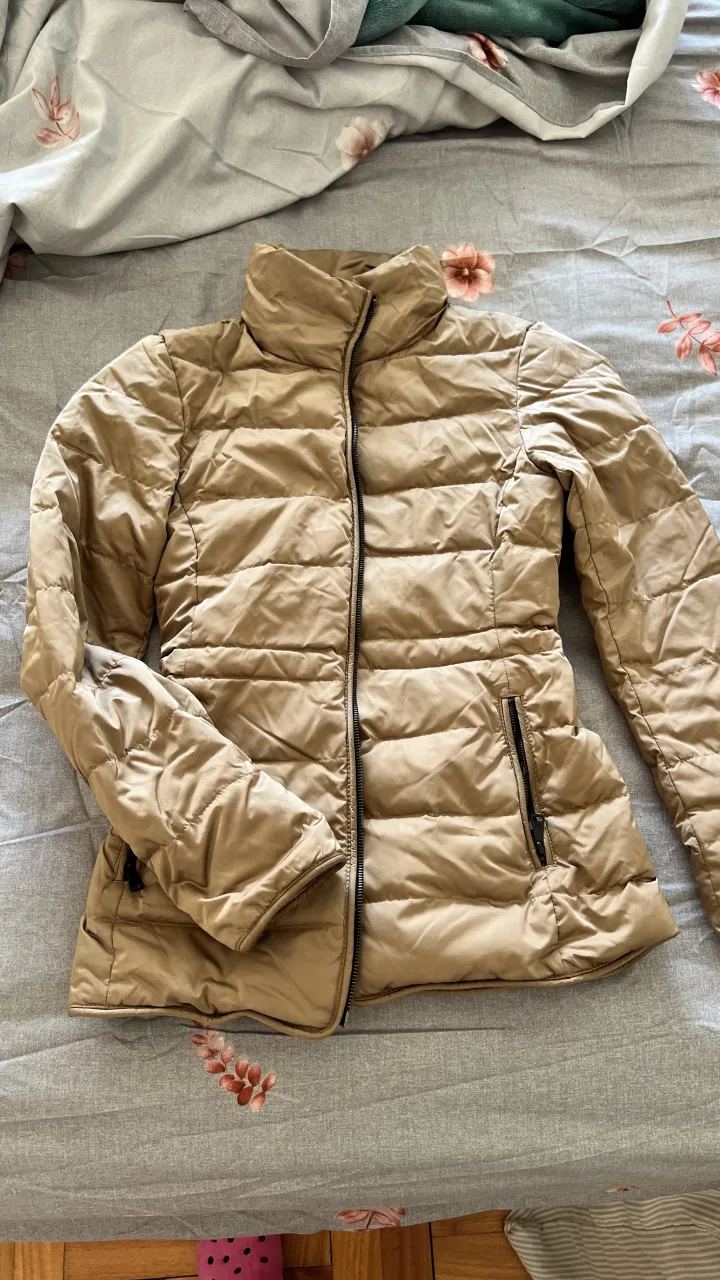 Campera de plumas dorada, súper abrigada y liviana. Ideal para los días fríos, con cuello alto y cierre al frente. Tiene bolsillos con cierre a los costados.