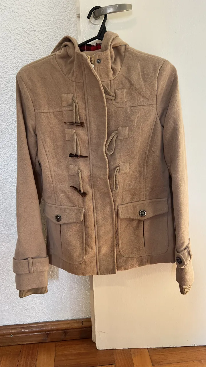 Campera taba con capucha, cierre y botones de madera. Tiene bolsillos con tapa y botones.