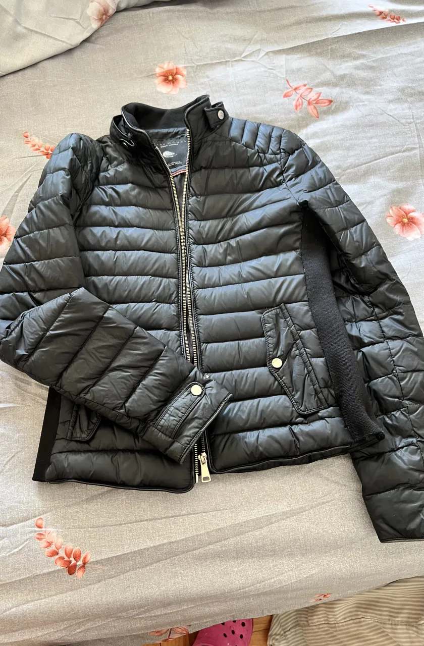 Campera de plumas negra, ideal para el frío. Tiene cierre al frente, bolsillos con botones y puños elastizados. Perfecta para un look casual y abrigado.