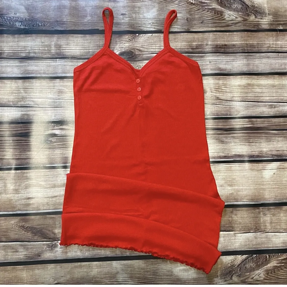 vestido roja de breteles finos con escote en V y detalles de botones. El borde inferior tiene un acabado ondulado.