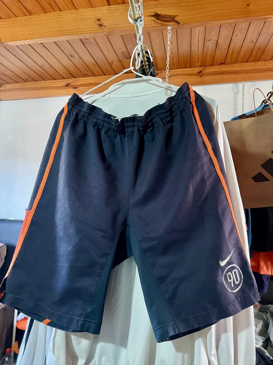 Shorts deportivos de color azul marino con detalles en naranja en los laterales. Posee logo de Nike y número 90 estampado en la pierna derecha. Año 2000
