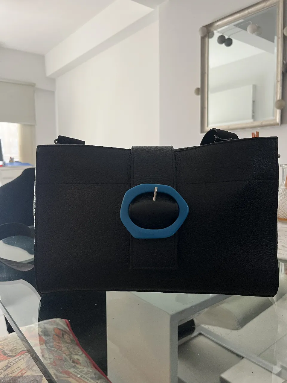 Cartera negra de cuero con hebilla azul. Diseño elegante y moderno, ideal para cualquier ocasión.