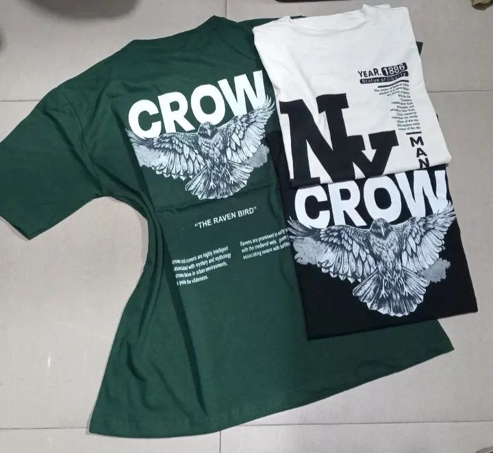Remera de hombre con estampado de cuervo y texto. Diseño oversize, ideal para un look urbano y moderno. Disponible en color verde oscuro y blanco.