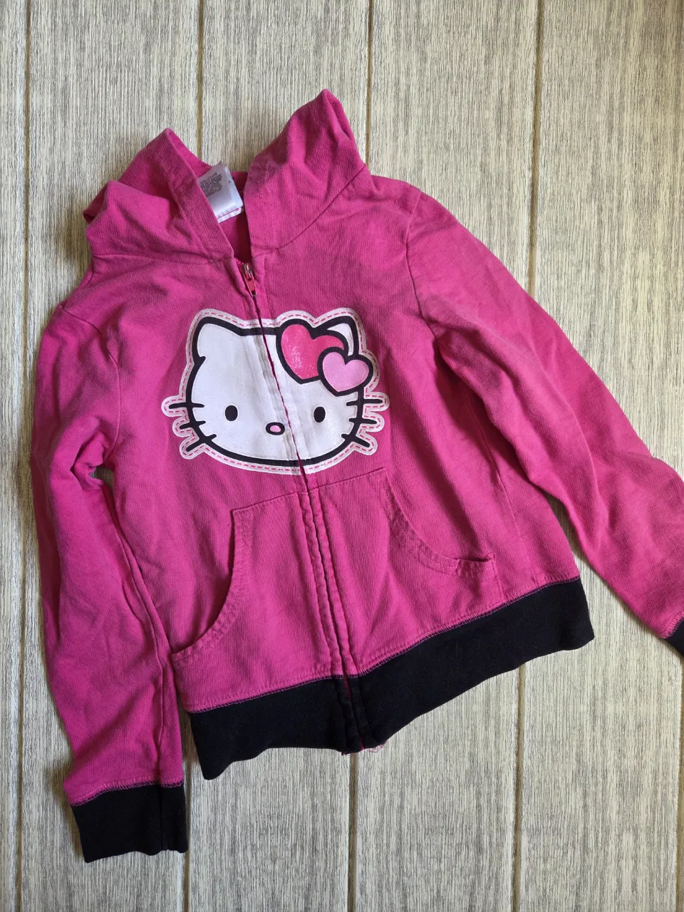 Buzo con capucha y cierre completo, color fucsia, con estampa de Hello Kitty en el frente. Posee bolsillos tipo canguro y puños y cintura de color negro.