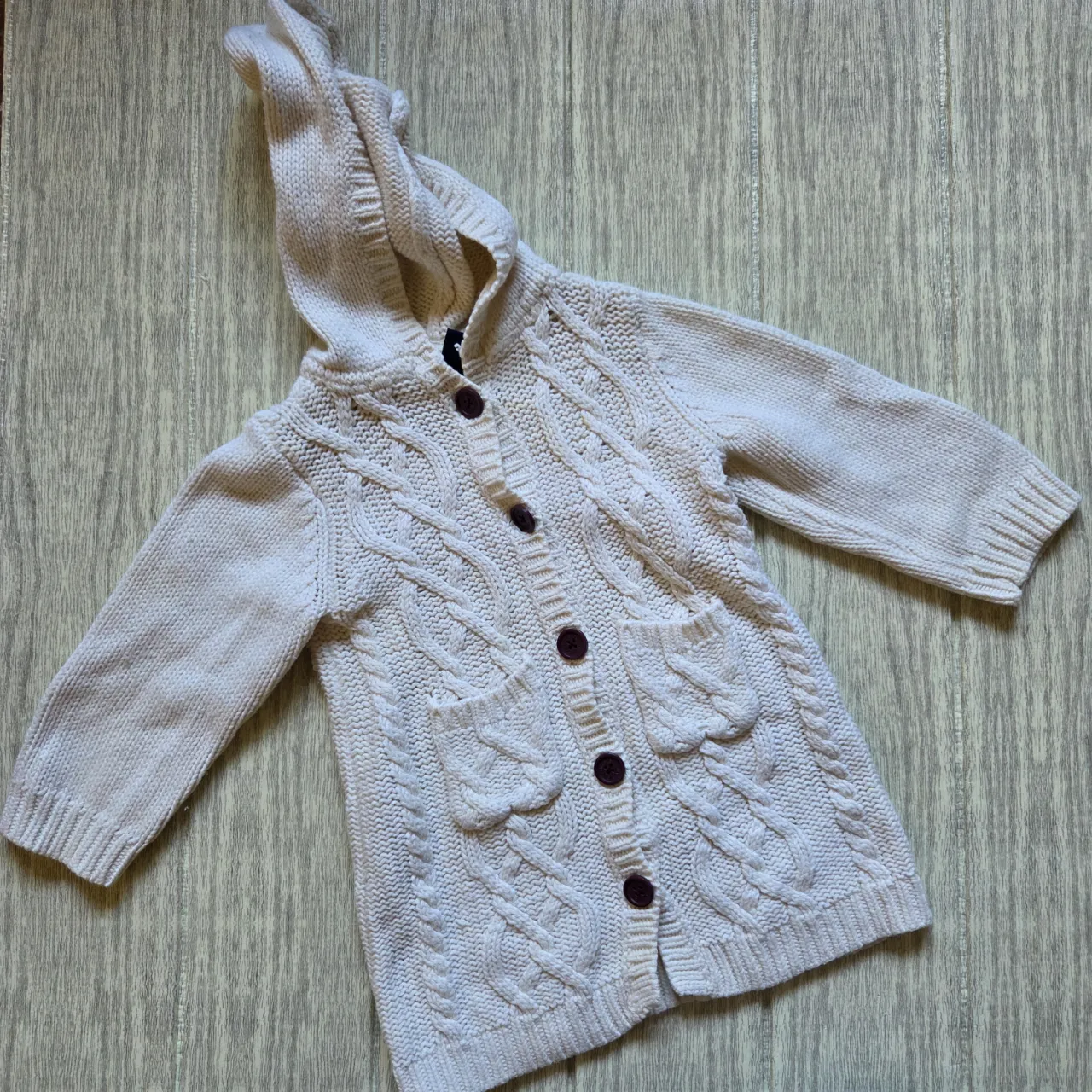 Cardigan de tejido de punto con trenzas, capucha y botones. Tiene dos bolsillos delanteros.