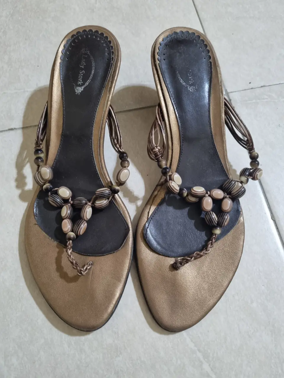 Sandalias doradas con detalles de cuentas marrones y beige. Diseño de dedo con taco bajo.