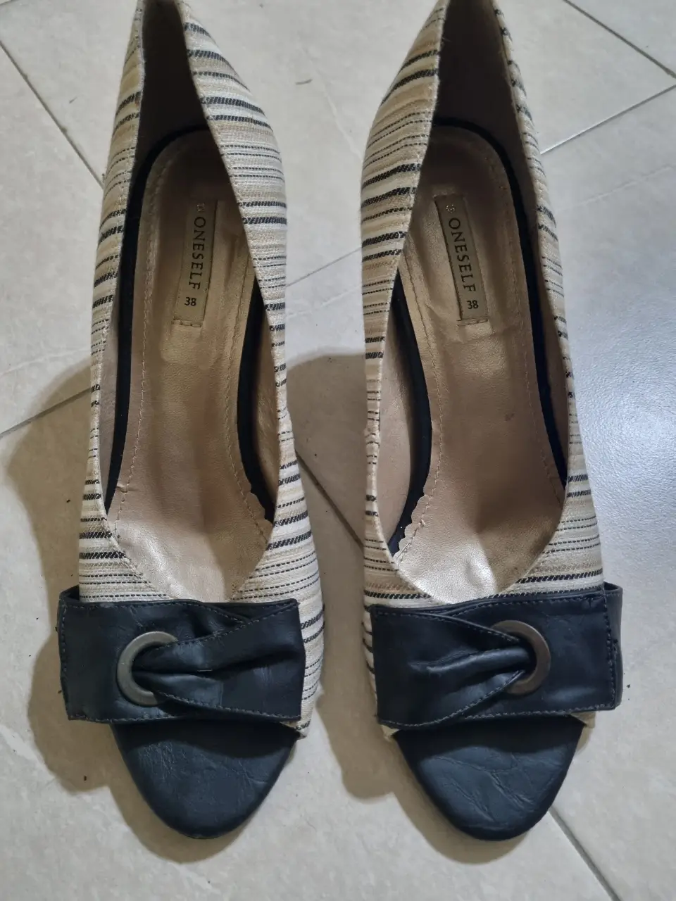Elegantes zapatos de tacón alto para mujer, con diseño a rayas en tonos crudo y negro. Detalles de moño y hebilla en la parte delantera, ideales para eventos formales o salidas nocturnas. Traídos de Brazil