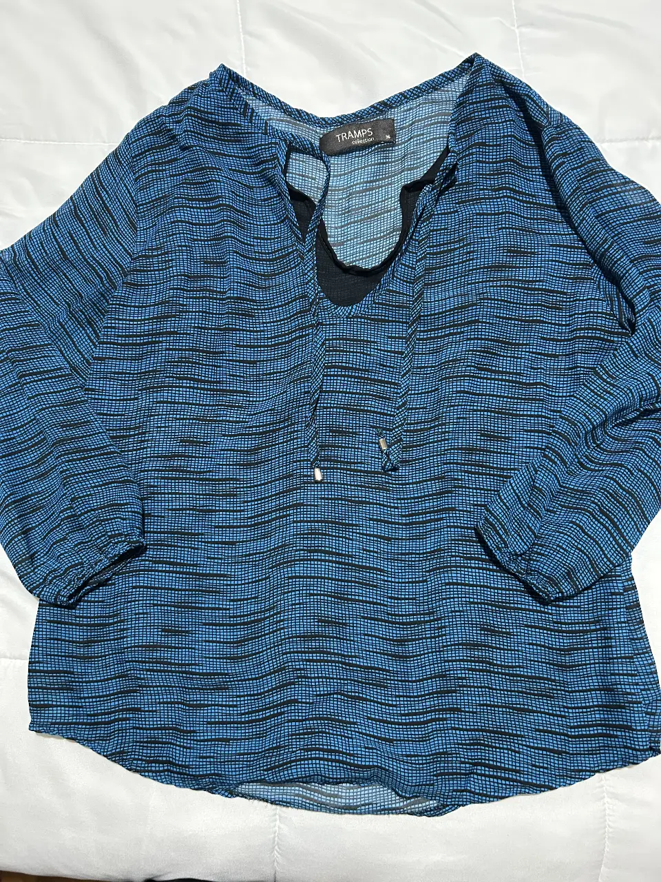 Blusa de mujer con estampado a cuadros en tonos azules y negros. Cuello en V con detalle de lazo y mangas 3/4. Ideal para un look casual y cómodo.