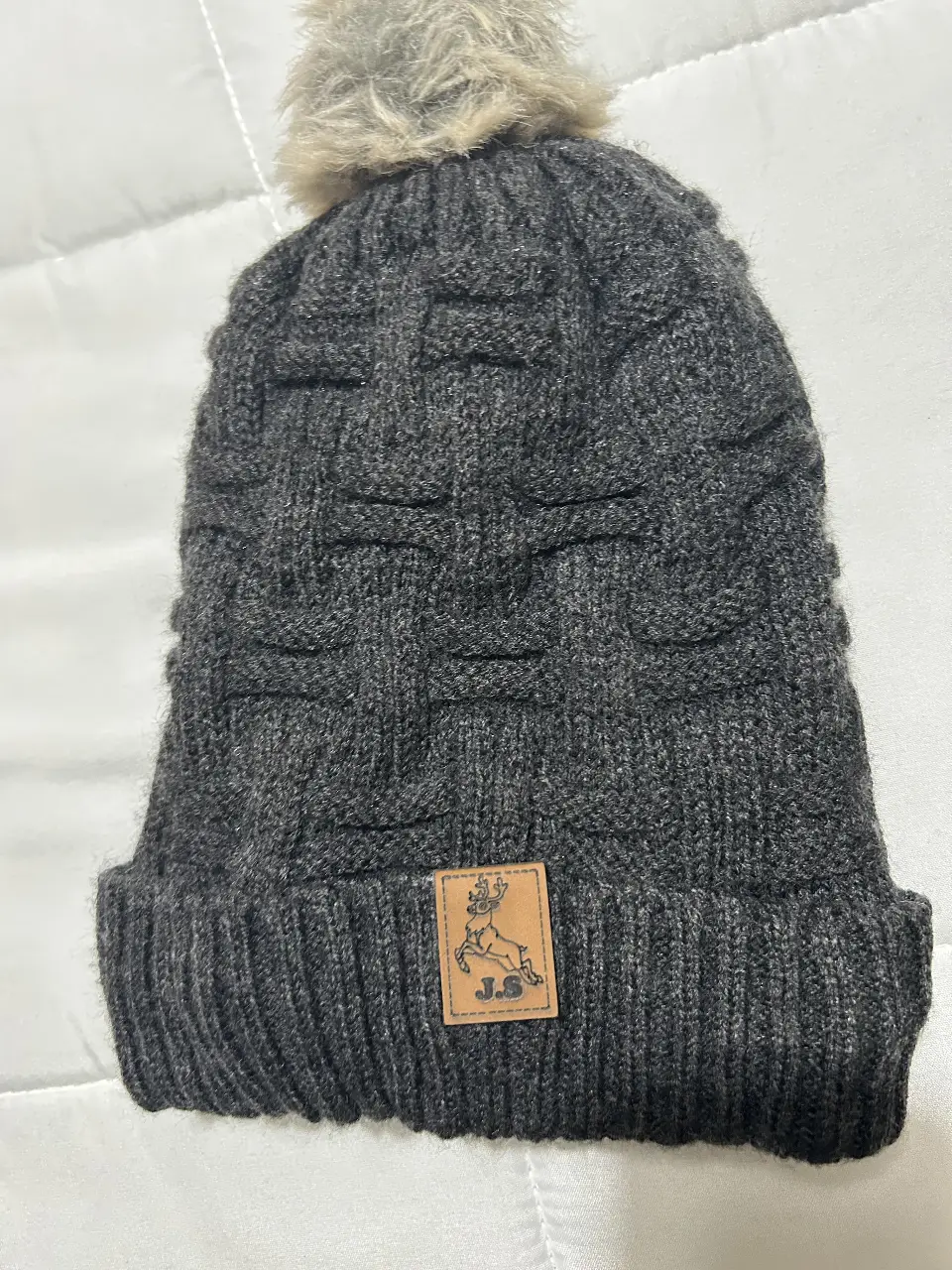 Gorro tejido de lana gris con pompón de piel sintética. Interior forrado en tela polar negra para mayor abrigo. Ideal para el invierno.