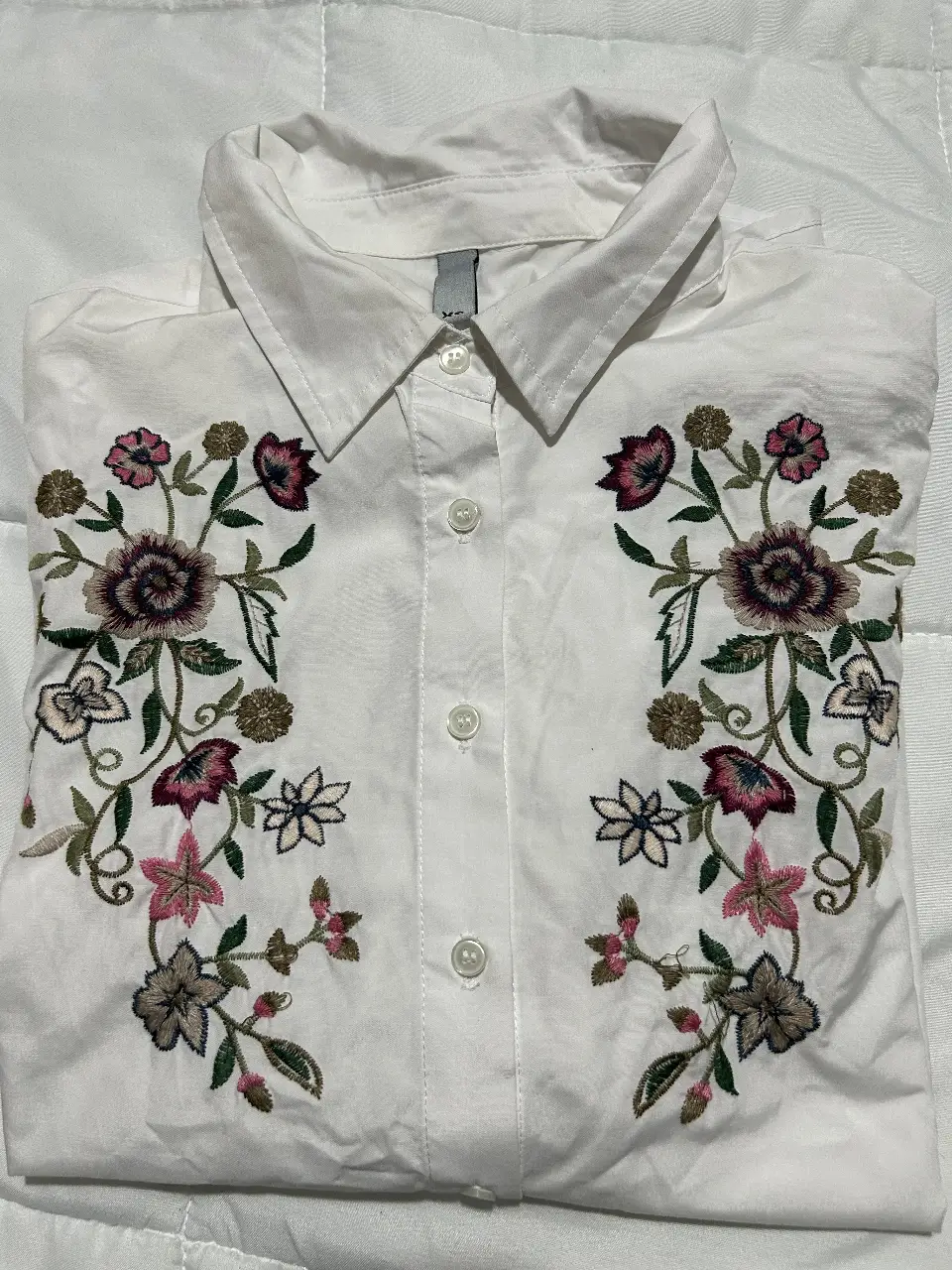 Camisa blanca manga larga de mujer con bordado floral en el frente con botón de recambio. Ideal para un look casual y fresco. 