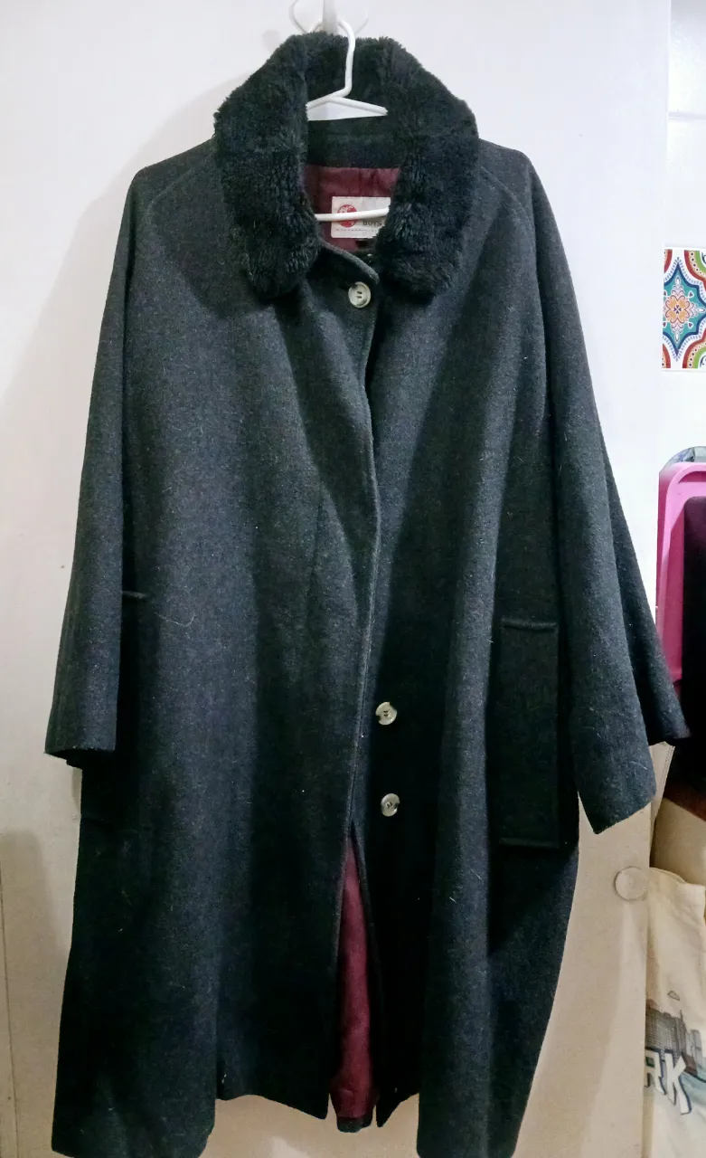 Tapado largo de paño gris oscuro con cuello de piel sintética negra. Posee botones y forro interior en color borgoña. Ideal para el invierno.